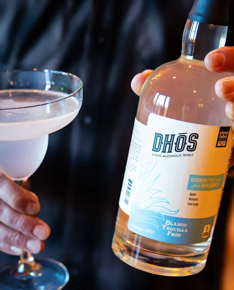 a person holding a bottle of Dhos non-alcoholic tequila and a margarita glass