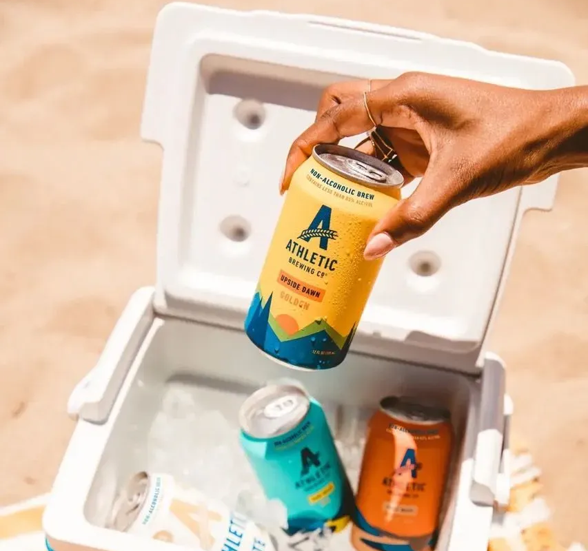 a person pulling an Athletic Company non-alcoholic beer out of a cooler